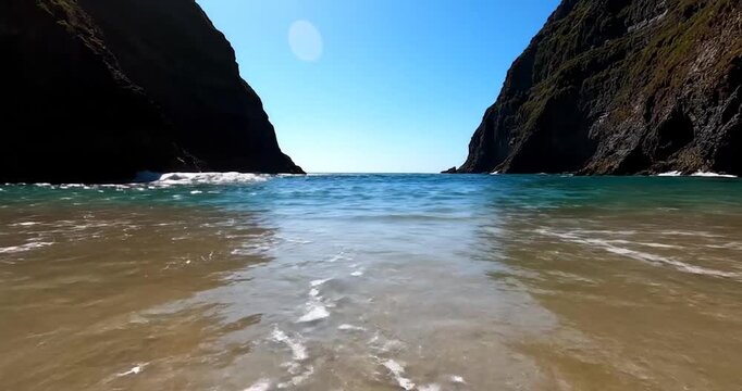 Waves washing onto sandy beach between two large sea cliffs