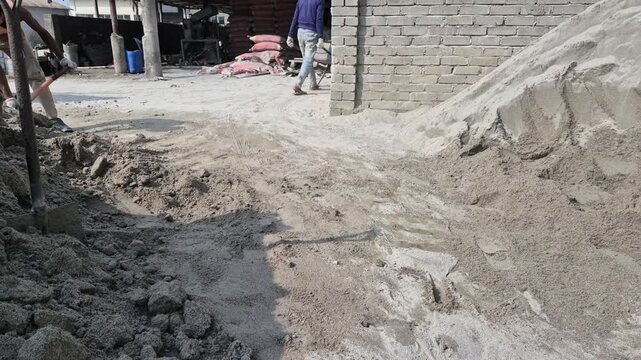 Professional RAW eye level wide shot of a worker pushing a sand-loaded trolley in an eco-brick factory in Bangladesh, 4K UHD 30fps.