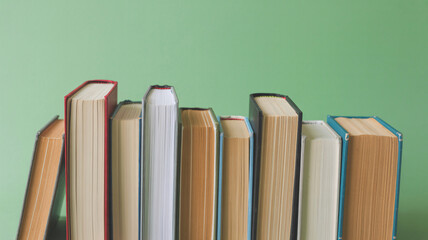 A row of various books with colorful spines standing upright against a plain green background, ready for reading.