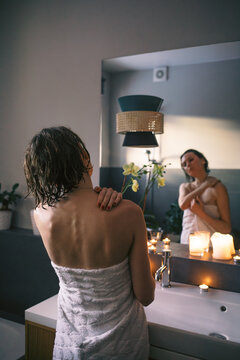 Woman in Towel Looking at Mirror in Candlelit Bathroom