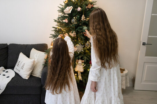 two girls are standing in dresses near the Christmas tree