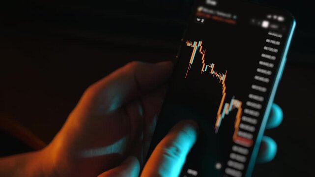 Close up of person analyzing financial candlestick chart on smartphone screen in dark environment.