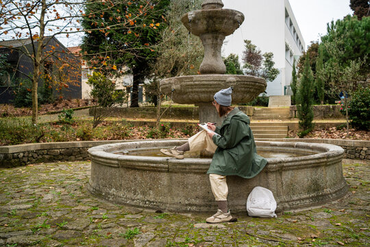 Woman sketching on notepad while sitting by a stone fountain in a park