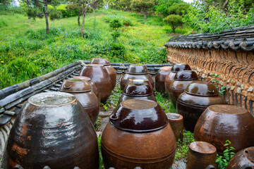 Obraz premium Traditional Korean jangdokdae earthenware jars arranged inside a traditional courtyard surrounded by greenery and stone walls.