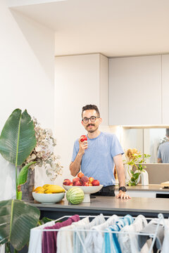Smiling man bites apple in a bright modern kitchen in Australia