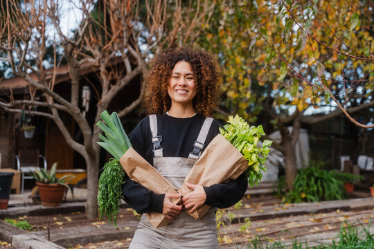Female Gardener With Harvested Celery And Leeks In Greenhouse Farm