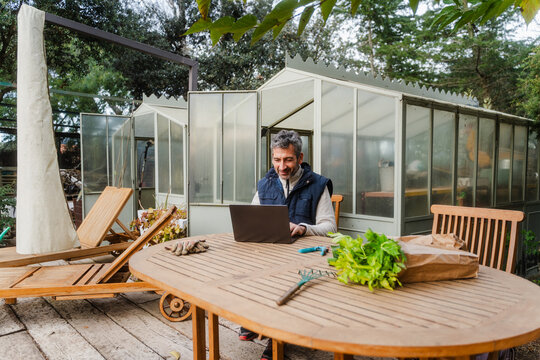 Male Owner Working On Laptop Near Greenhouse Storage