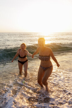 two women running away from a wave on a beach
