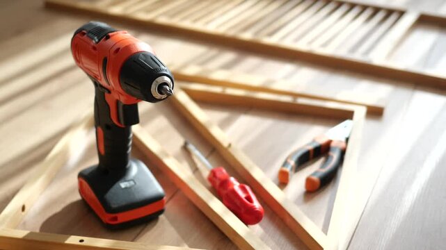 Close up video of cordless drill, screwdriver, pliers and wooden frames on light wooden floor in a sunny room, ready for assembly work
