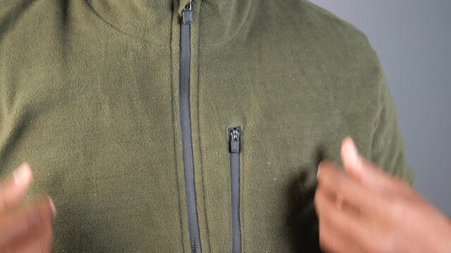 Person zipping up olive green fleece jacket over t-shirt, close up shot