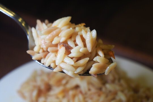 Orzo pasta served on a spoon with a dish in background