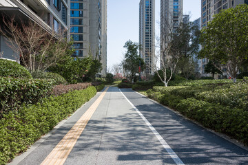 A shaded pedestrian pathway in a modern residential area flanked by high-rise buildings and lush greenery © zhu difeng