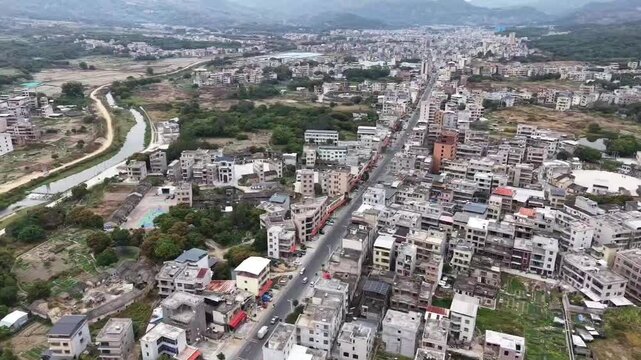 Cinematic aerial shot of a bustling Chinese town showing traditional circular earthen buildings (Tulou) standing alongside modern residential blocks. Contrast between old and new China.