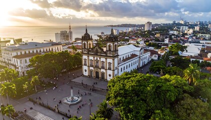 Fototapeta premium Aerial view of a coastal city with a large, ornate cathedral and plaza under a golden sunset sky
