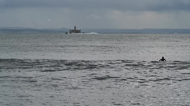 Person standing in ocean water near Bugio lighthouse