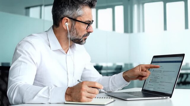 Focused Businessman Taking Notes While Working on Laptop in Modern Office.