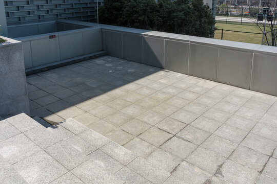 Modern rooftop terrace with gray stone tiles and low concrete walls under sunlight