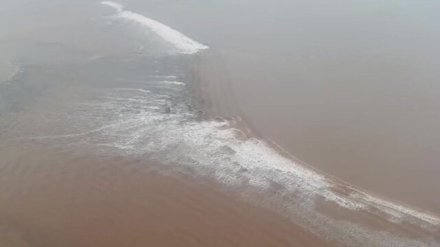 Spectacular aerial shot of the Qiantang River tidal bore, showing the intersection of powerful waves and muddy water currents. A rare natural phenomenon in Zhejiang, China.