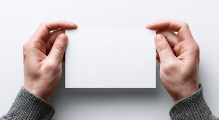 Two hands holding a blank white rectangular card against a plain white background
