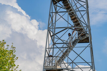 Woman ascends metal staircase against blue sky with clouds.