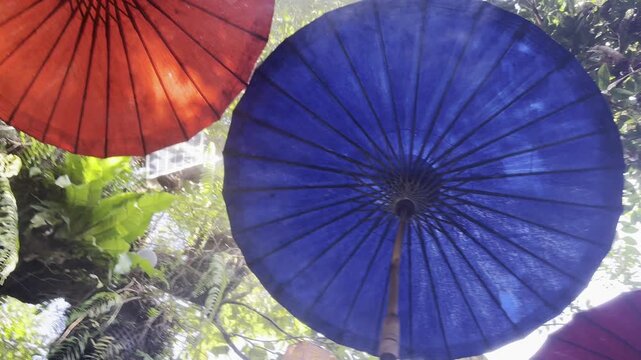 purple red and blue umbrella hanging among trees in a forest style garden, decoration with colourful lanterns, mist in the sky, setting for a celebration