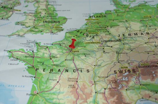 A man's hand is sticking a red pushpin into Paris, capital city and largest city of France, on a geographical map of Europe.