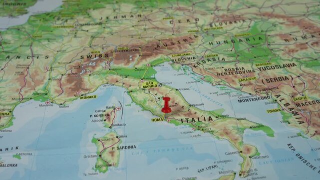 A woman's hand is sticking a red pushpin into the city of Rome, Capital and largest city of Italy, on a geographical map of Europe.