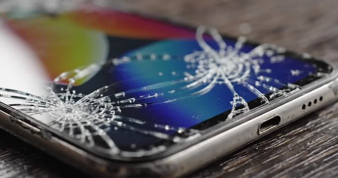 Close-up of a cracked smartphone screen with spiderweb-like fractures on a wooden surface