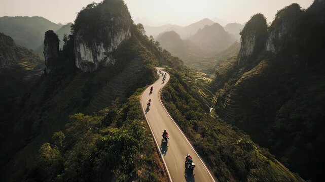 A motorcycle convoy navigates a winding mountain road through lush, terraced hills and dramatic peaks