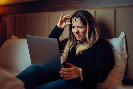 Woman Squinting and Lifting Her Glasses to Read on the Screen. Lady with blurred vision lifting spectacles to read small text on a digital monitor 
