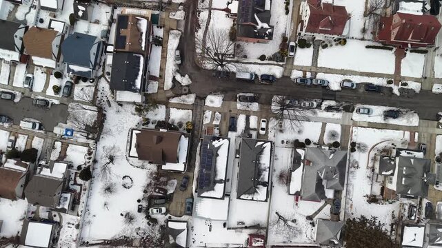 Aerial lookdown drone footage flying over a suburban residential neighborhood in queens, new york city, showing houses, streets, and cars blanketed in white snow during a cold winter day