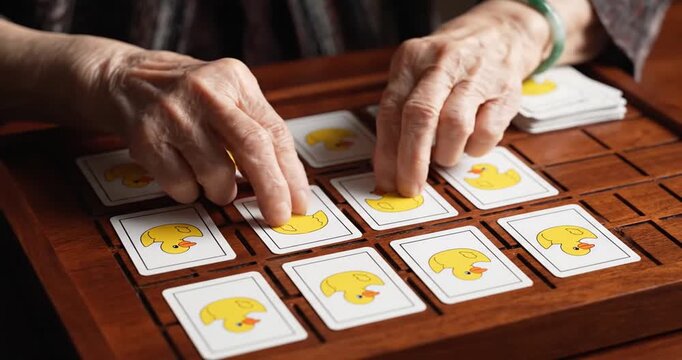 Elderly hands engaged in a memory card game featuring yellow duck illustrations on a wooden board