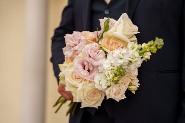 Groom holds a bouquet of white and pink flowers during a wedding ceremony in a garden at daytime