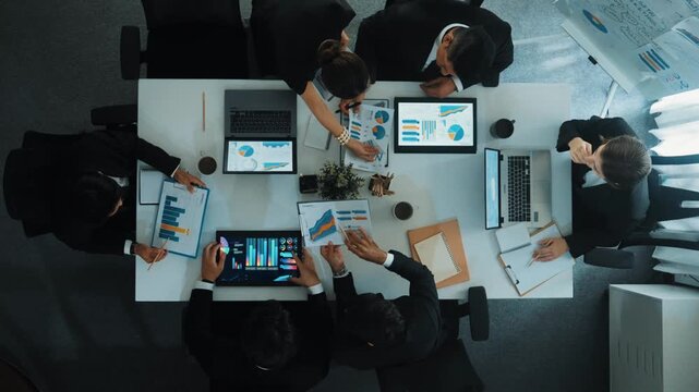 Top down aerial view of smart business woman handing out financial document to diverse team while discuss or brainstorm about marketing strategy with investment chart display on tablet. Directorate.