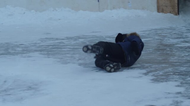 Happy child in winter parka and ushanka hat sliding and falling on ice at outdoor rink. Cheerful boy laughing and enjoying active winter games on a frozen pond