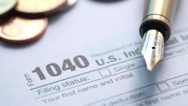 Close up view of fountain pen on 1040 tax return form with coins and blurred background