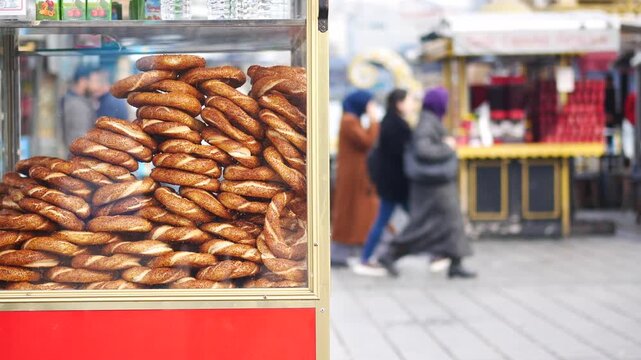 Fresh turkish simit bagels stacked in red street food cart with blurred people walking in background in istanbul