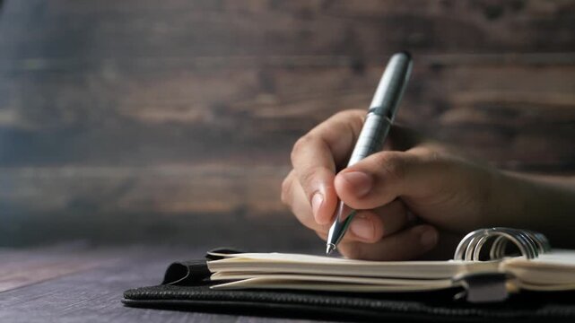 Close-up of hand holding pen and writing in notebook, business and education concept