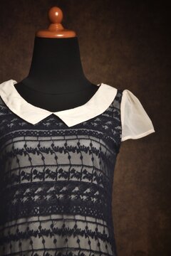 Outer black lace mini dress with white collar and beige inner in close-up on a display mannequin