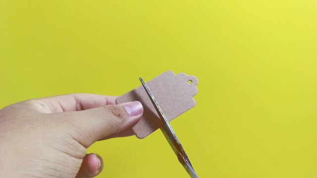 Hand cutting a price tag, suggesting impulsive buying and discount offers on a bright yellow background, promoting sales