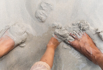 child and parent playing with wet sand beside bare feet on beach © explorewithinfo