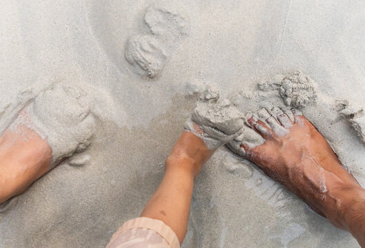 child and parent playing with wet sand beside bare feet on beach