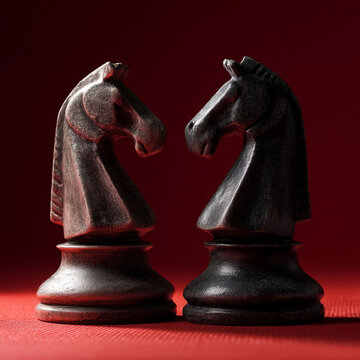 Two dark wooden chess knights facing each other on red background