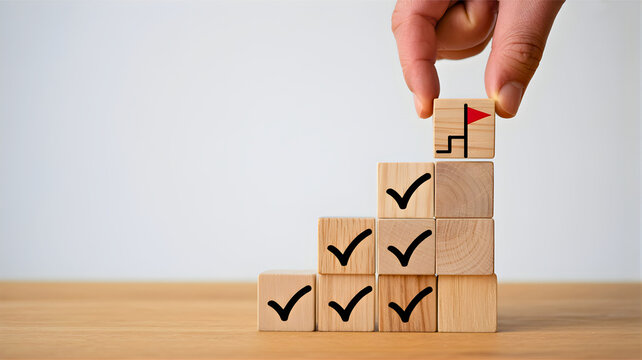 Hand placing last block on a wooden block stack with check marks on a wooden surface against a white wall, reference 22.jpg