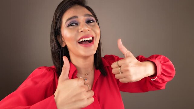 Close up of happy laughing joyful young Asian woman lady look at camera show thumbs up sign with hands fingers gesture like, nice, recommend advertising isolated over grey studio background.