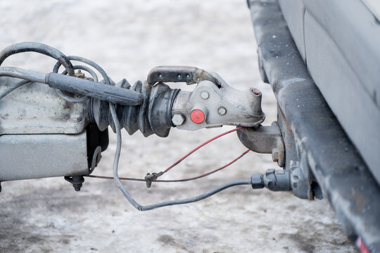 Metal trailer hitch connection with coupler latch, safety wire and electrical cable attached to car tow bar, winter road surface background in daylight