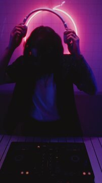 DJ turning the buttons, dancing. Man playing music on electronic mixer controller at disco club. Male disk jockey mixing sound on set, night club. Turntable panel. Clubbing vibe, neon party. Vertical
