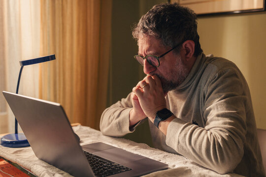 Senior man reviewing financial information on laptop at home with concerned expression