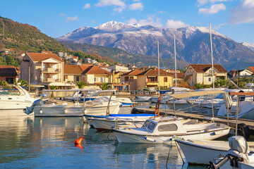 Obraz premium Fishing boats in harbour. Mediterranean landscape on sunny winter day. Montenegro. View of marina Kalimanj in Tivat city. Snow-capped Lovcen mountain