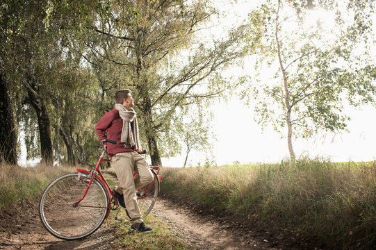 Young man with bicycle on dirt road through trees
